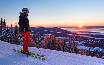Une skieuse en ski alpin prend une pause et observe le coucher du soleil au sommet d'une montagne au Mont-Sainte-Anne.