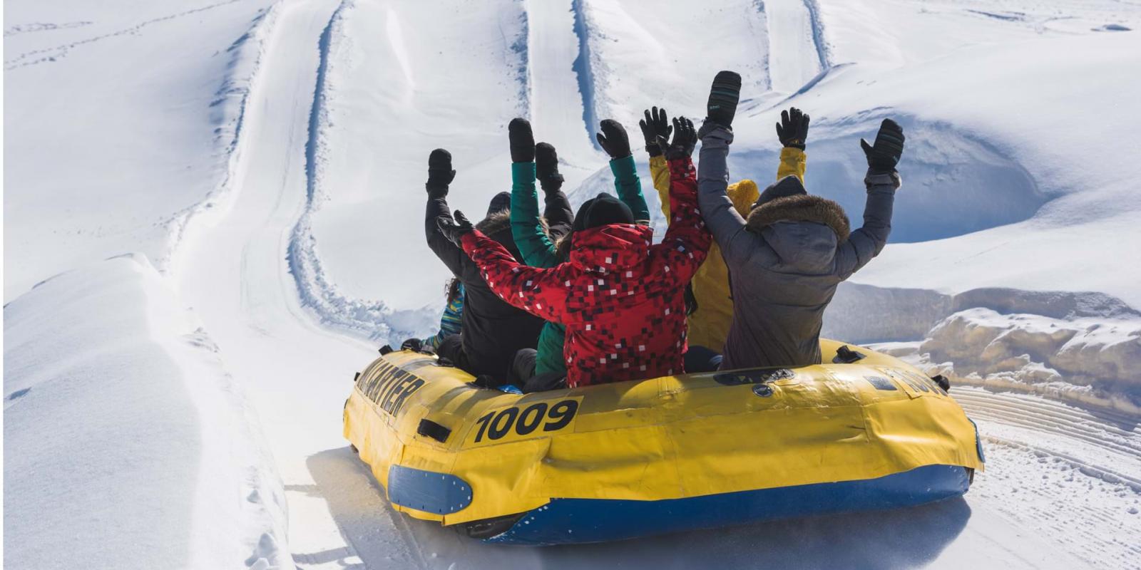Un groupe fait du rafting sur neige, les bras dans les airs, dans une glissade du Village Vacances Valcartier.