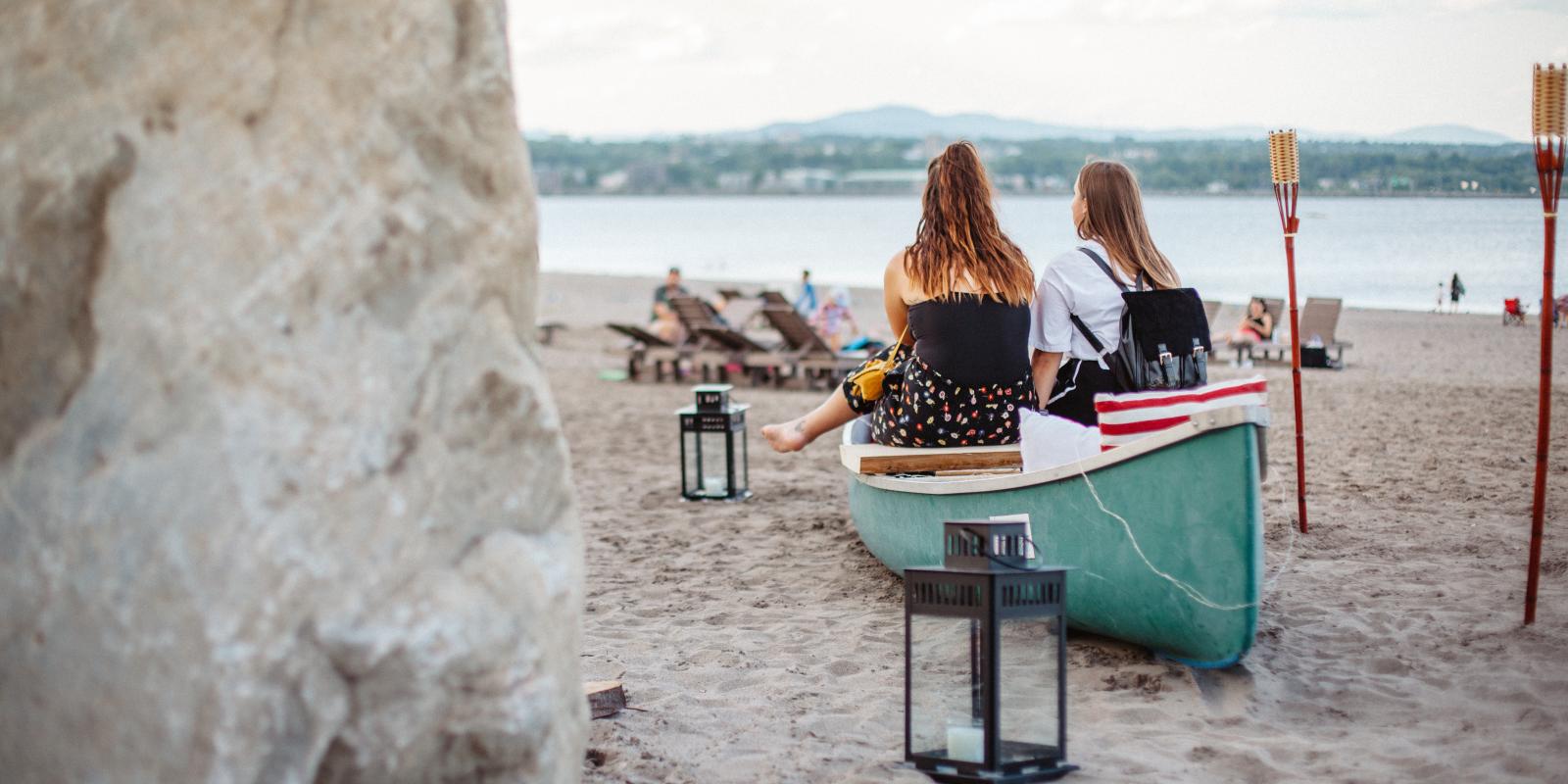 Two girls relax near a canoe on the beach at Baie de Beauport.
