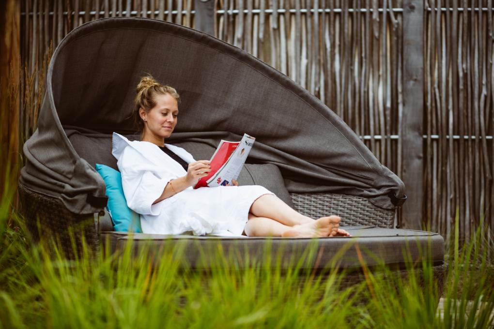 Une femme lit un magazine sur la terrasse extérieure de l'Aroma Spa au Village Vacances Valcartier.